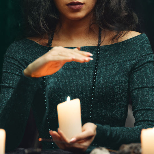 A person holding a candle with one hand, while hovering over the flame with their other hand